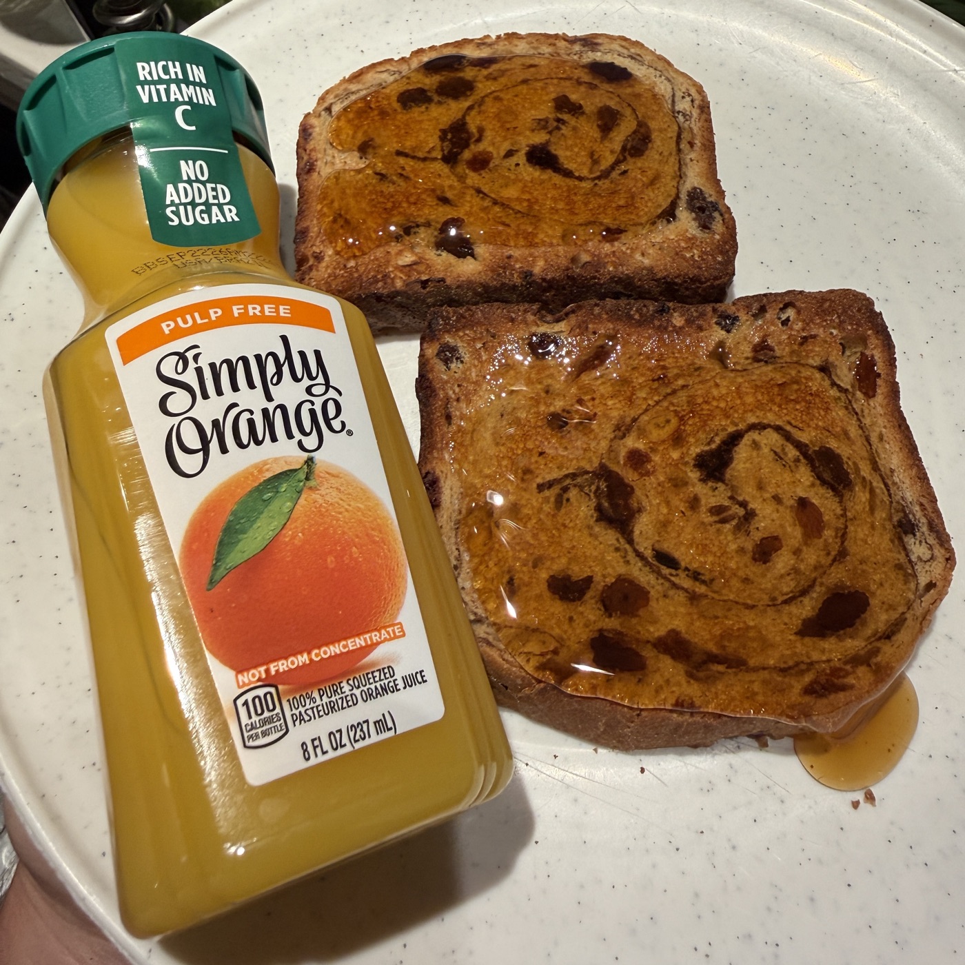 Loading-day evening snack: two slices of cinnamon-raisin bread drizzled with maple syrup on a speckled plate, next to a small bottle of Simply Orange juice.